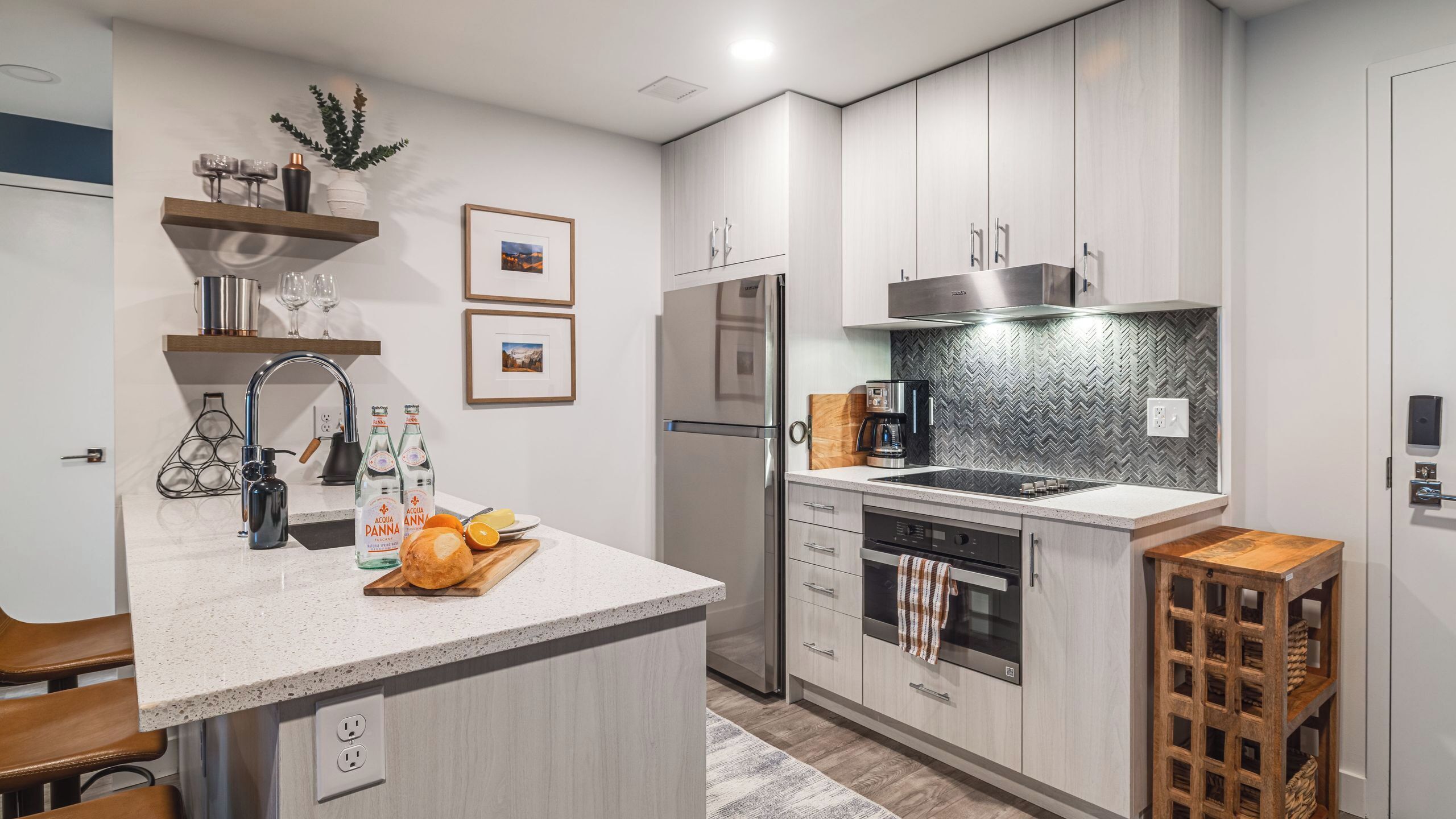 A modern kitchen with a central island, stainless steel appliances, and a herringbone backsplash.
