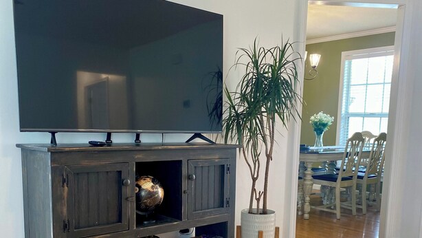 Un salon avec un grand téléviseur à écran plat fixé sur un meuble en bois foncé, des paniers en osier et une plante en pot.
