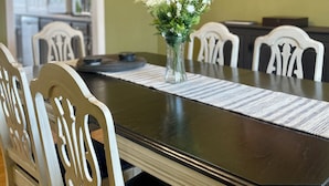Une salle à manger avec une table en bois foncé, des chaises blanches et un vase rempli de fleurs.