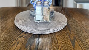 Une cuisine avec une table en bois, agrémentée d’un ensemble de salière et de poivrière, d’un coq en céramique bleue décorative et d’un ventilateur de plafond.