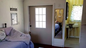 Ein Schlafzimmer mit einem Bett, einem Nachttisch mit Buch und Stift, einem Fenster und einer Tür zu einem Badezimmer.