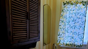 Ein Badezimmer mit gestreifter Wand, einem Holzkästen, einem Spiegel, einem Waschbecken und einem Fenster mit Blumenmuster-Vorhang.