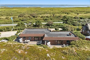 Un bâtiment à deux étages, doté d’un toit plat, d’une terrasse avec des meubles d’extérieur et offrant une vue sur la mer.