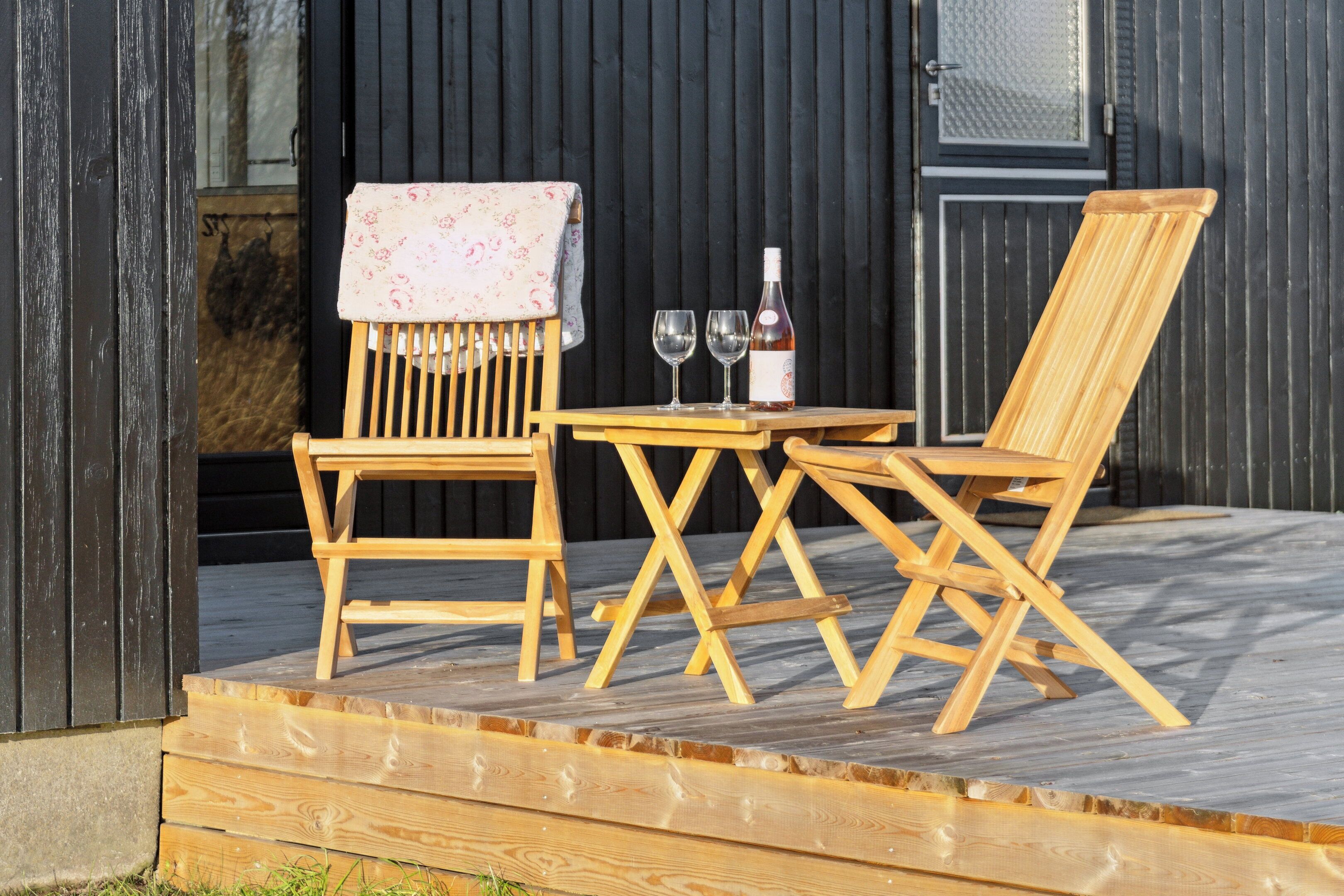 A wooden outdoor seating area with a table and two chairs, a bottle of wine, and two glasses.