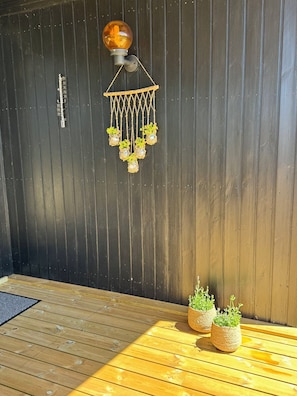 A wooden deck with a hanging light fixture and potted plants. - Cozy summer house close to beach and nature (Rønde)