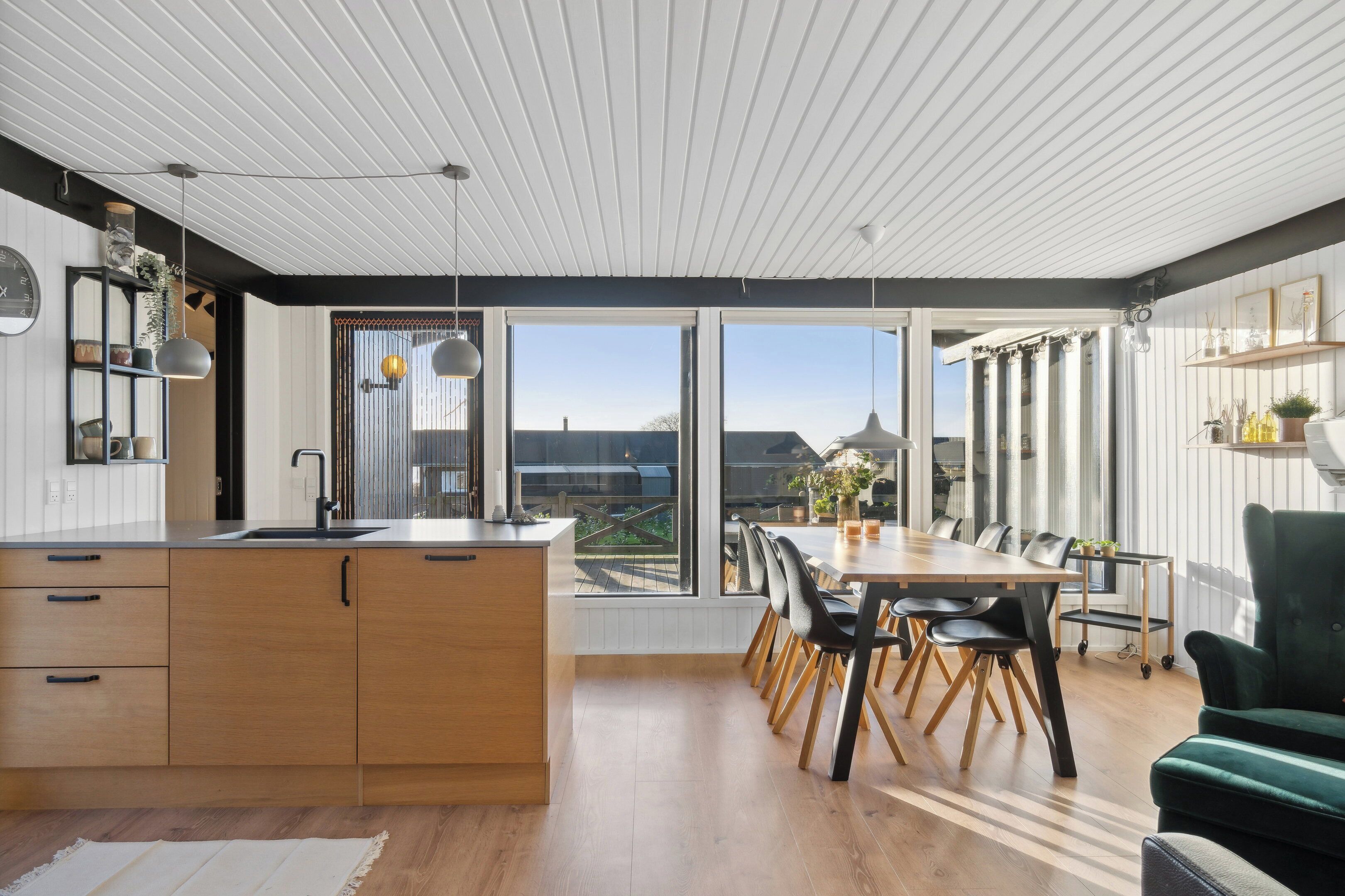 A modern kitchen with a large island, dining area with chairs, and a view through large windows.