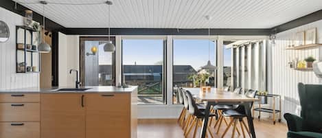 A modern kitchen with a large island, dining area with chairs, and a view through large windows.