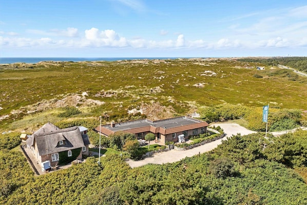 A coastal property with a main building and a detached house, surrounded by greenery and a clear view of the sea.