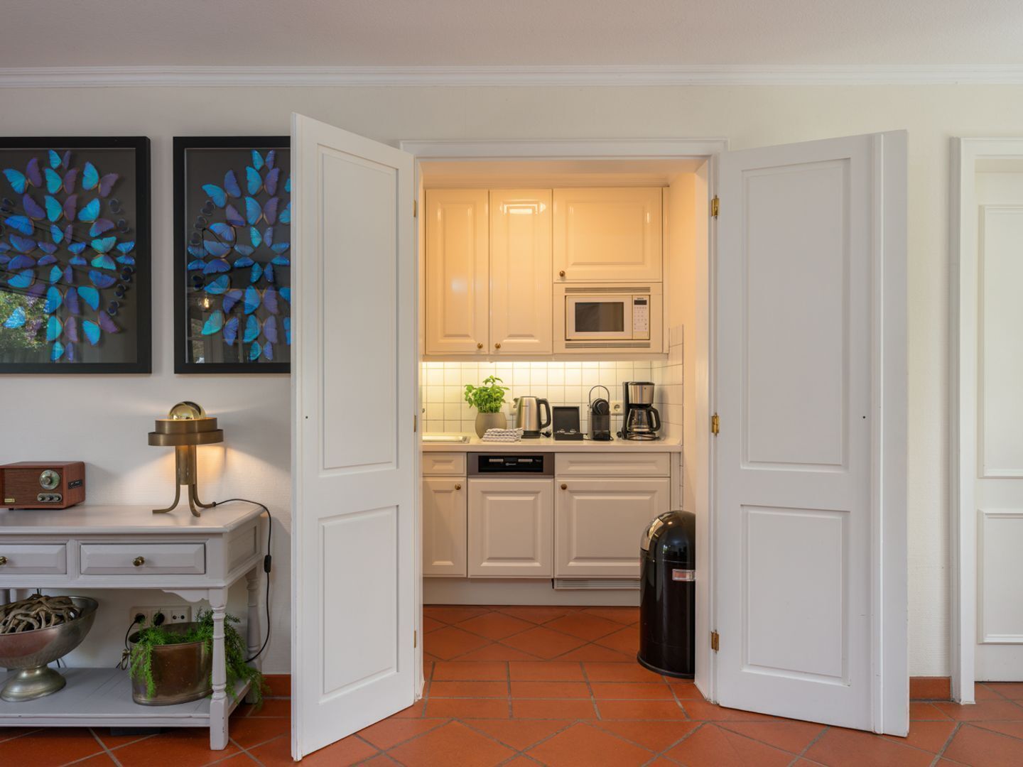 A kitchen with white cabinets, a microwave, a coffee maker, and a trash can.