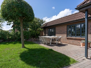 A patio with a table and chairs, a brick building with windows, and a tree.