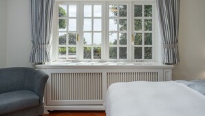 A room with a large window, a radiator, a grey armchair, and a bed. - Beach Bungalow Sylt 1 - Welcome to your private paradise in the middle of the (Sylt OT Rantum)