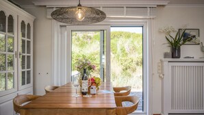 A dining area with a wooden table, chairs, a hanging light fixture, and a view through a glass door to the outdoors. - Beach Bungalow Sylt 1 - Welcome to your private paradise in the middle of the (Sylt OT Rantum)