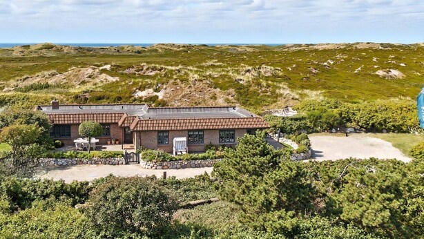 A two-story building with a flat roof, a stone foundation, and a patio area with outdoor seating. - Beach Bungalow Sylt 1 - Welcome to your private paradise in the middle of the (Sylt OT Rantum)
