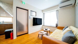 A modern hotel room with a wooden floor, a bed with a yellow and white checkered blanket, a flat-screen TV mounted on the wall, a small round table with a chair, and a window with curtains. - SHIRAKABA (Otaru)