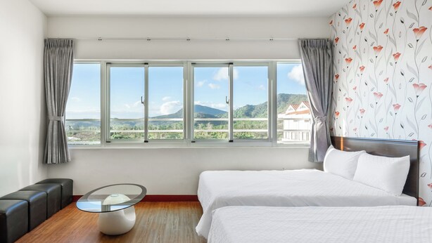 A hotel room with a large window, two beds, a glass coffee table, and a seating area with a sofa and armchairs. - Rich house (Hengchun)