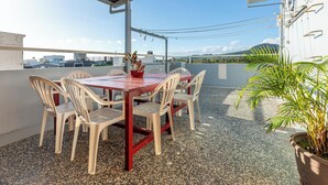 A covered outdoor dining area with a table and chairs, a potted plant, and a view of buildings and mountains in the background. - Rich house (Hengchun)