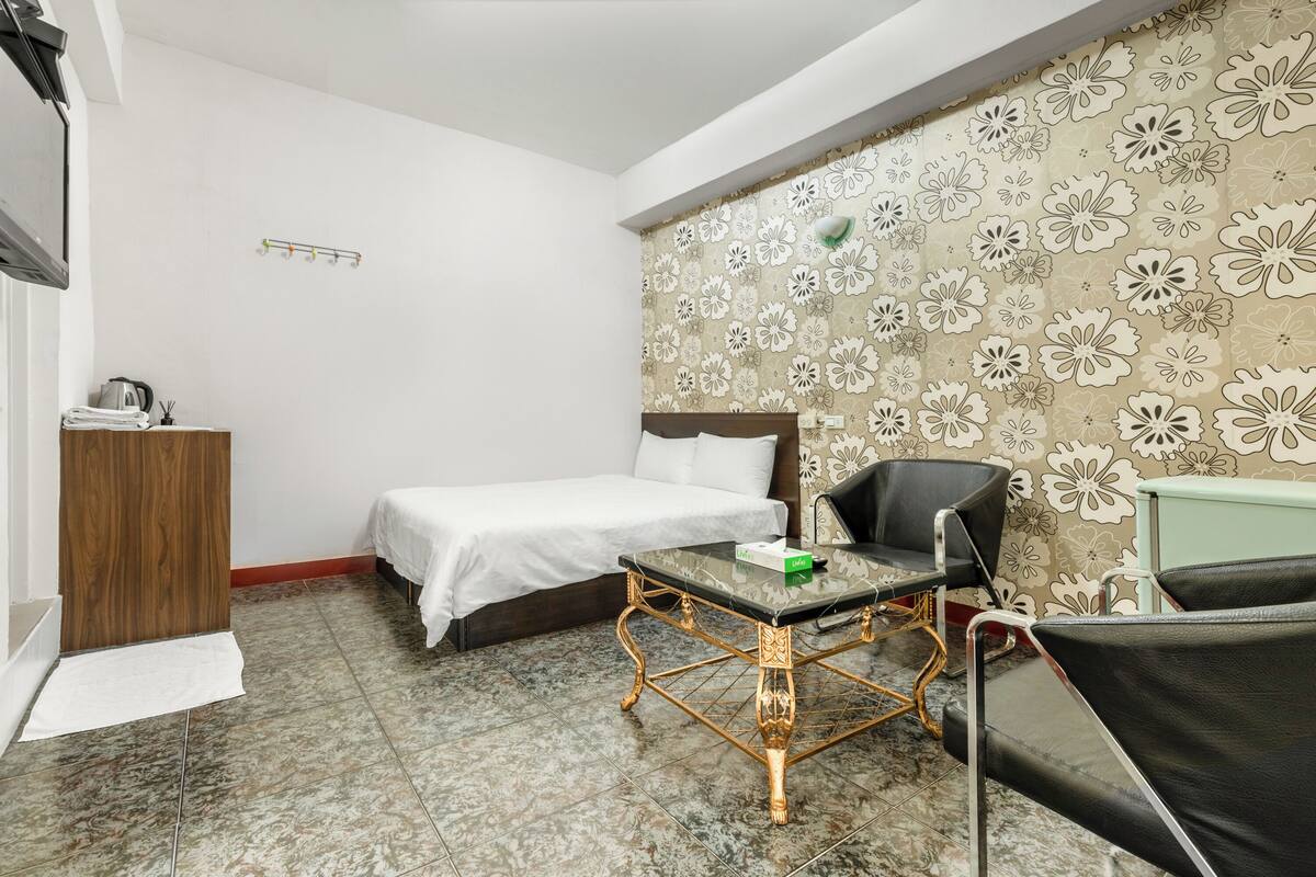 Ein Hotelzimmer mit Bett, Schreibtisch, Stuhl und Wandpapier mit Muster.