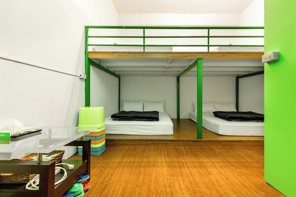 Un dormitorio con literas, una pequeña mesa con una cesta y una pared verde.