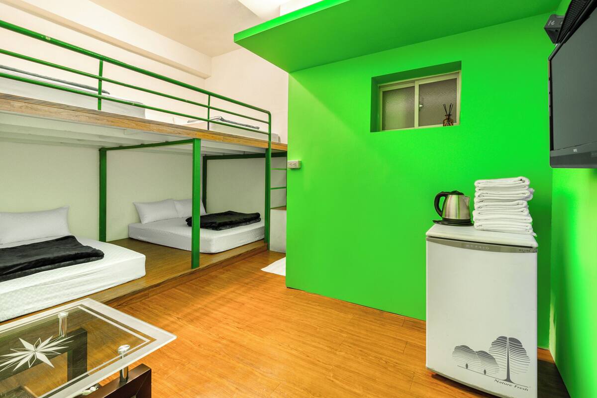 Ein Schlafsaalzimmer mit Etagenbetten, einer kleinen Küchenzeile und einer Wand in Grünton.