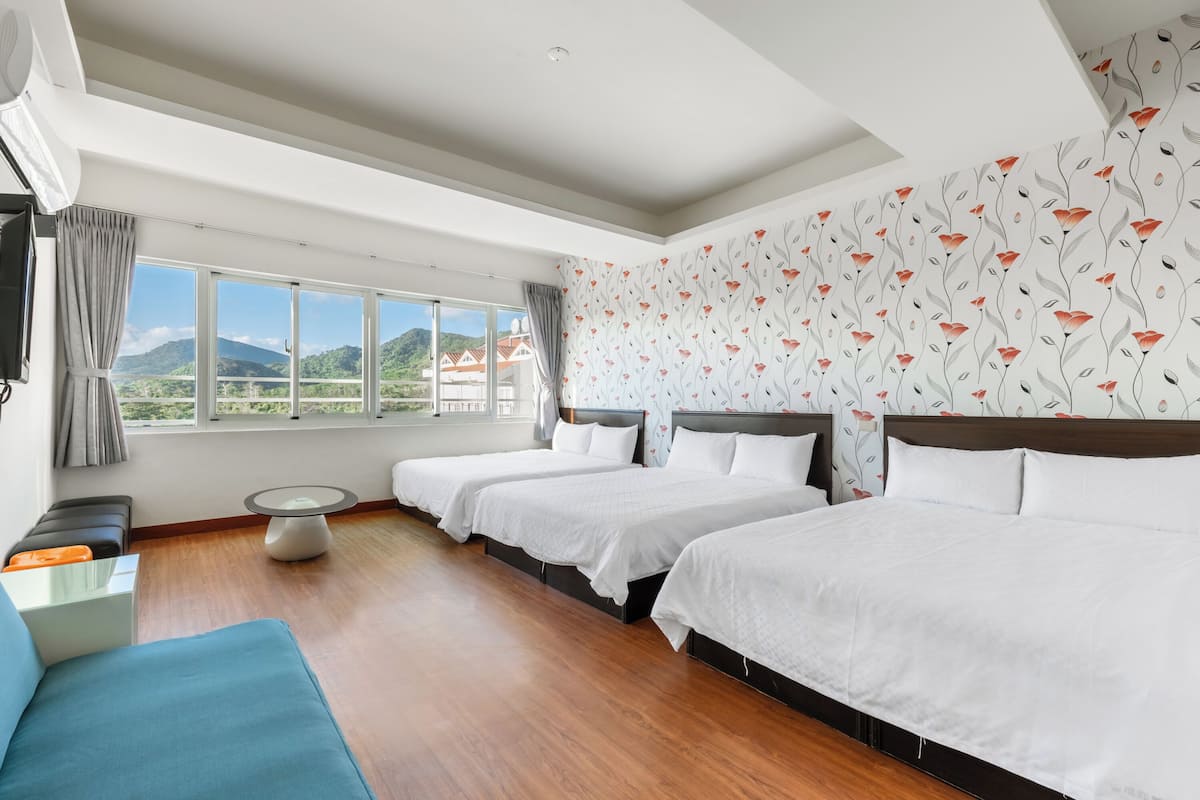 Ein Hotelzimmer mit zwei Betten, einem Sofa, einem kleinen Tisch und einem großen Fenster mit Bergblick.