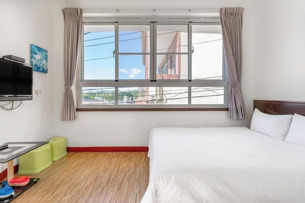 A hotel room with a large window, a bed, a TV, and a small table with slippers.