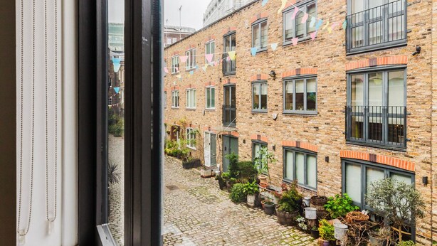 A courtyard with a brick building, potted plants, and a cobblestone path. - Blueground | Fitzrovia, nr museum & park, w/d (London)