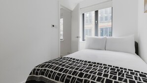 A bedroom with a bed, white walls, a window, and a door. - Blueground | Fitzrovia, nr museum & park, w/d (London)