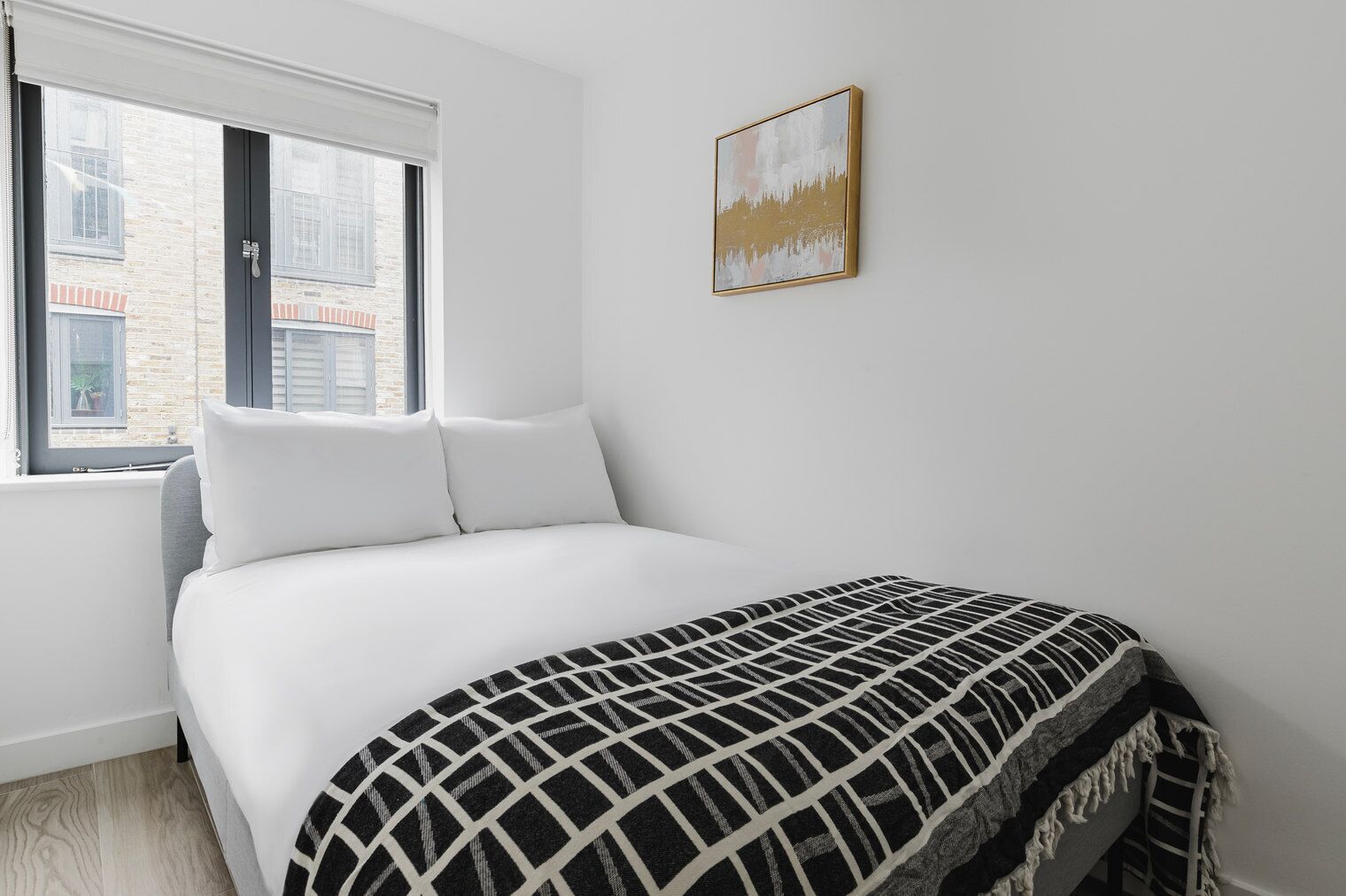 Quarto com uma cama, paredes brancas, uma janela e um quadro.