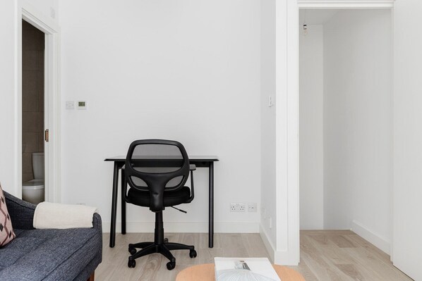 A modern, minimalistic room with a grey sofa, a black office chair, and a small table.