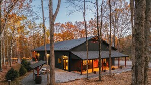 A rustic cabin with a large porch, surrounded by trees and a gravel path. - Luxury Barndominium w/ Golf Sim, Hot Tub, Home Theater, Minutes to Jim Thorpe! (Jim Thorpe)