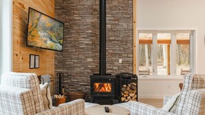 A cozy living room with a stone fireplace, plaid furniture, and a painting on the wall. - Luxury Barndominium w/ Golf Sim, Hot Tub, Home Theater, Minutes to Jim Thorpe! (Jim Thorpe)