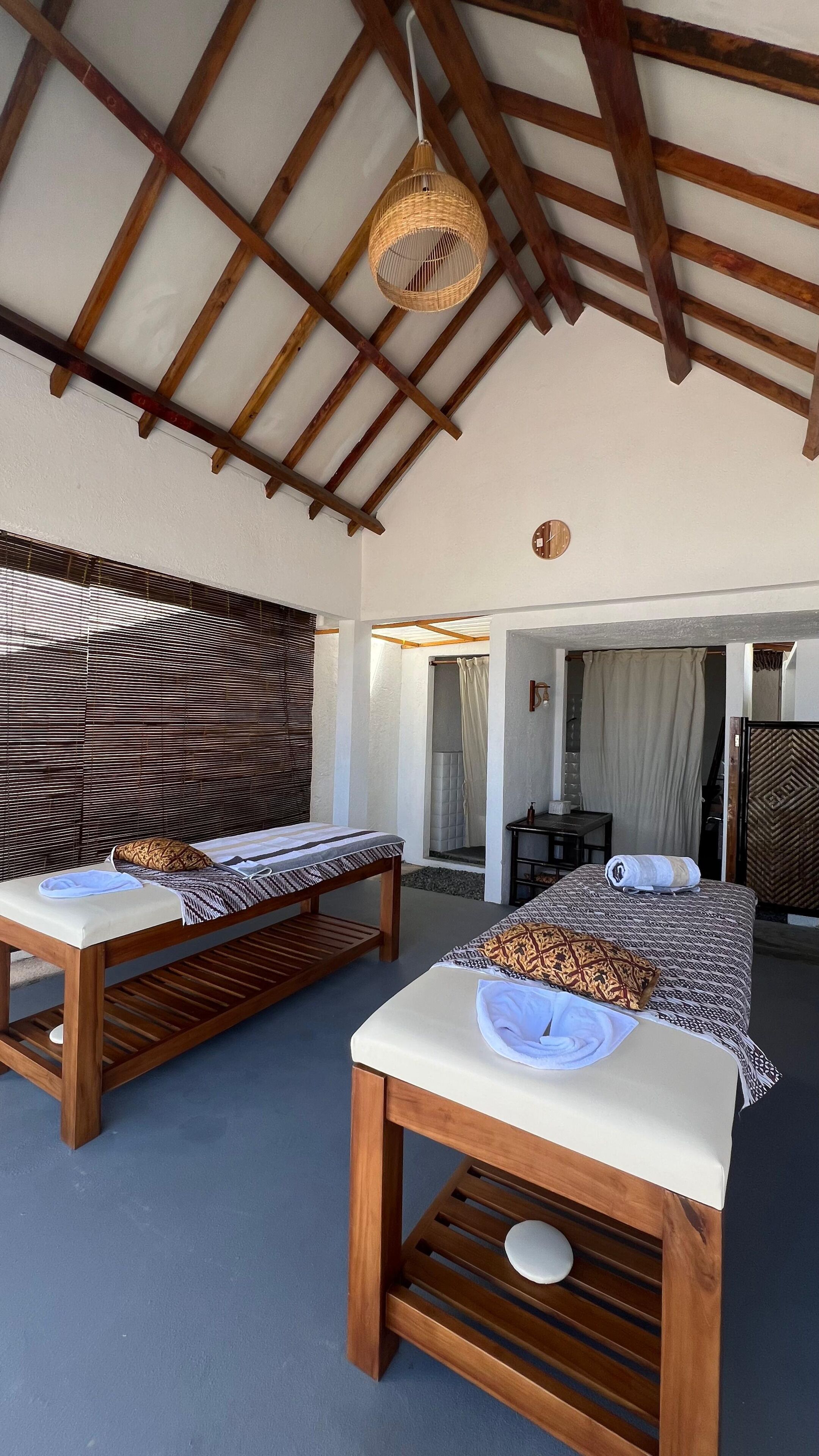 A room with two wooden beds, a ceiling fan, and a large window with blinds.