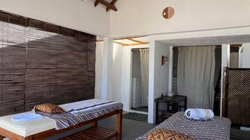 A room with two wooden beds, a ceiling fan, and a large window with blinds.