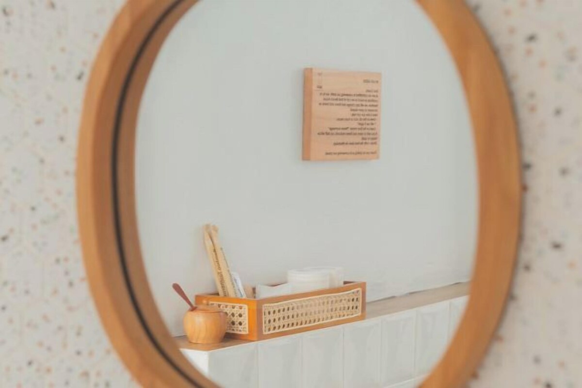 A mirror with a wooden frame reflecting a wall-mounted sign and a small wooden shelf with a cup and a pen.