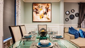 Un coin repas avec une table en verre dressée pour quatre personnes, entourée de chaises, avec un canapé et des œuvres d'art décoratives au fond.