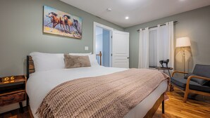 Une chambre à coucher avec un grand lit, une table de chevet avec une horloge, une chaise, une lampe et un tableau au mur.