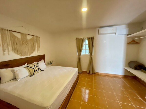 A bedroom with a bed, a headboard, a wall-mounted air conditioner, and a window with curtains. - Arrecife Suite (Isla Mujeres)