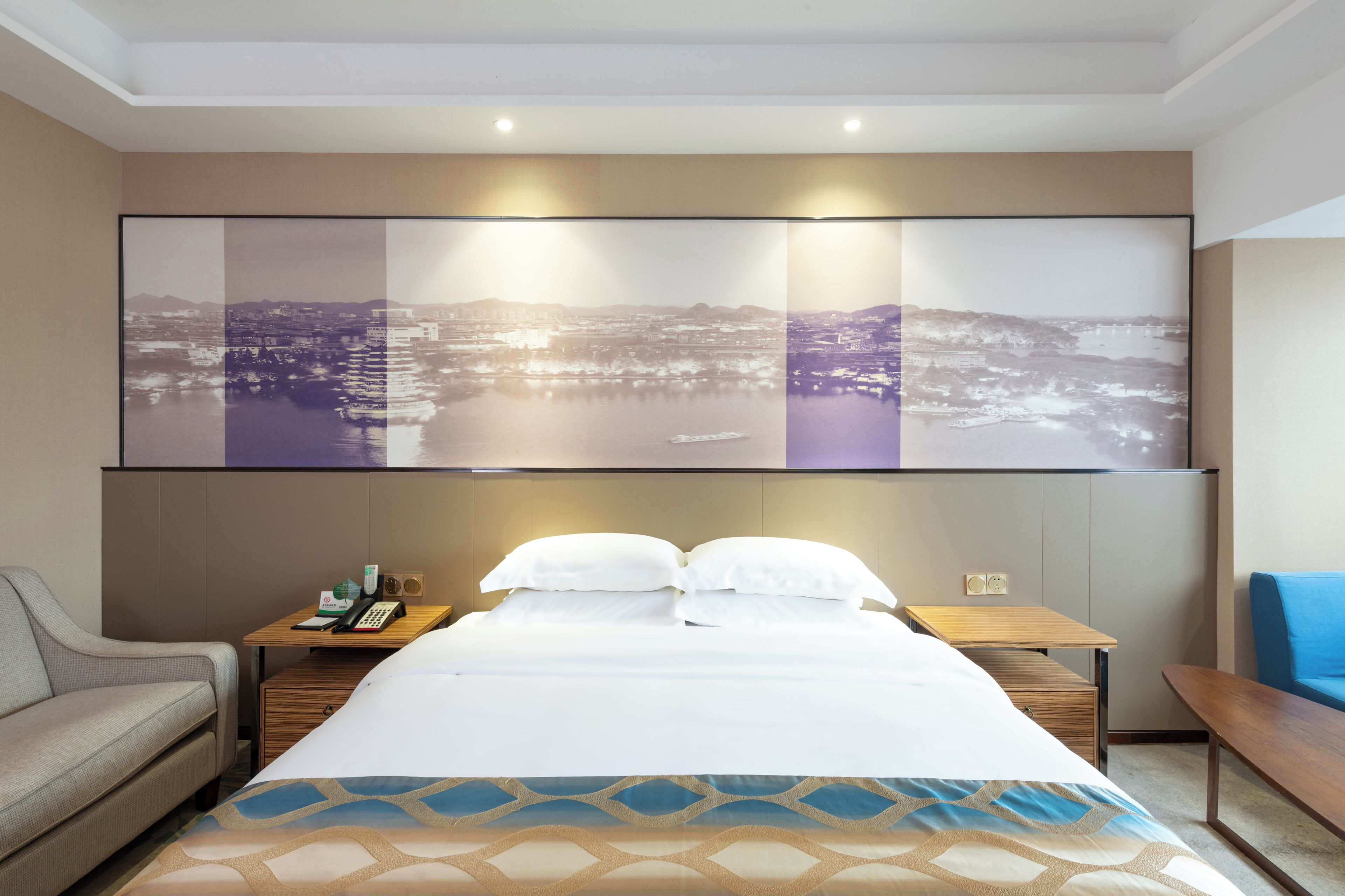 Quarto de hotel com cama, mesa de cabeceira, abajur e uma grande obra de arte com vista para a cidade na parede.