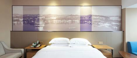 Quarto de hotel com cama, mesa de cabeceira, abajur e uma grande obra de arte com vista para a cidade na parede.