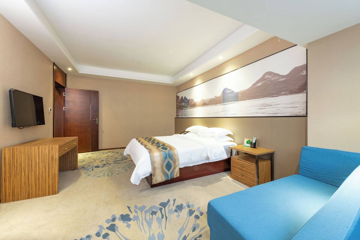 Una habitación de hotel con una cama, un escritorio, un televisor y un cuadro en la pared.