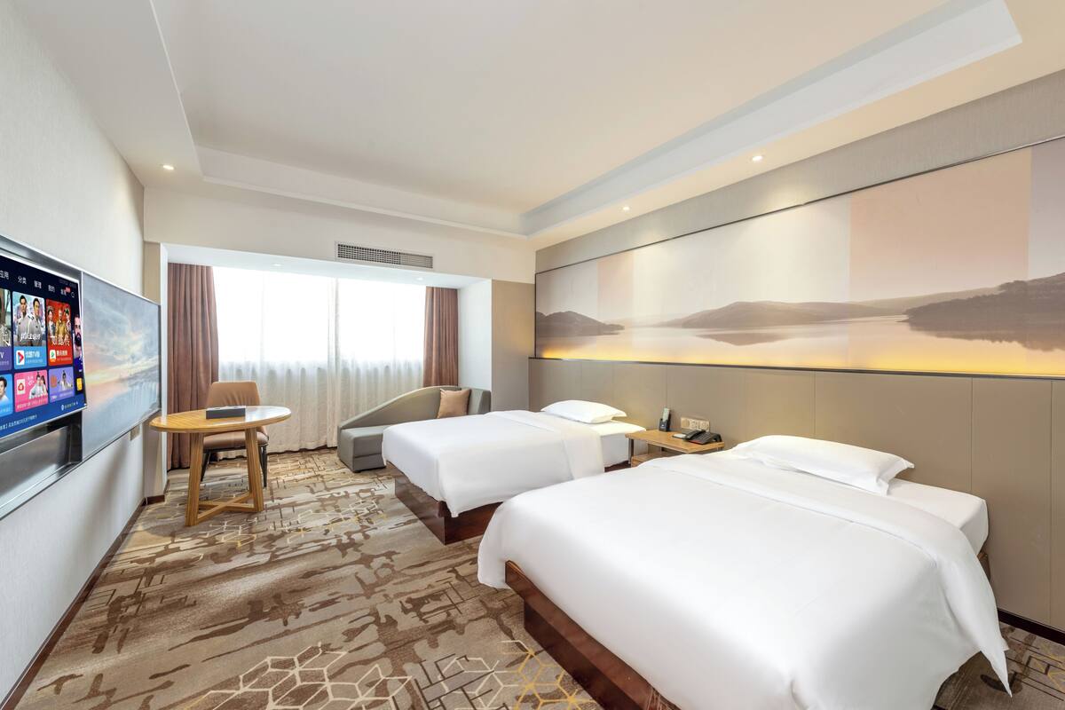 Habitación de hotel con dos camas, un escritorio, un televisor y un ventanal grande.