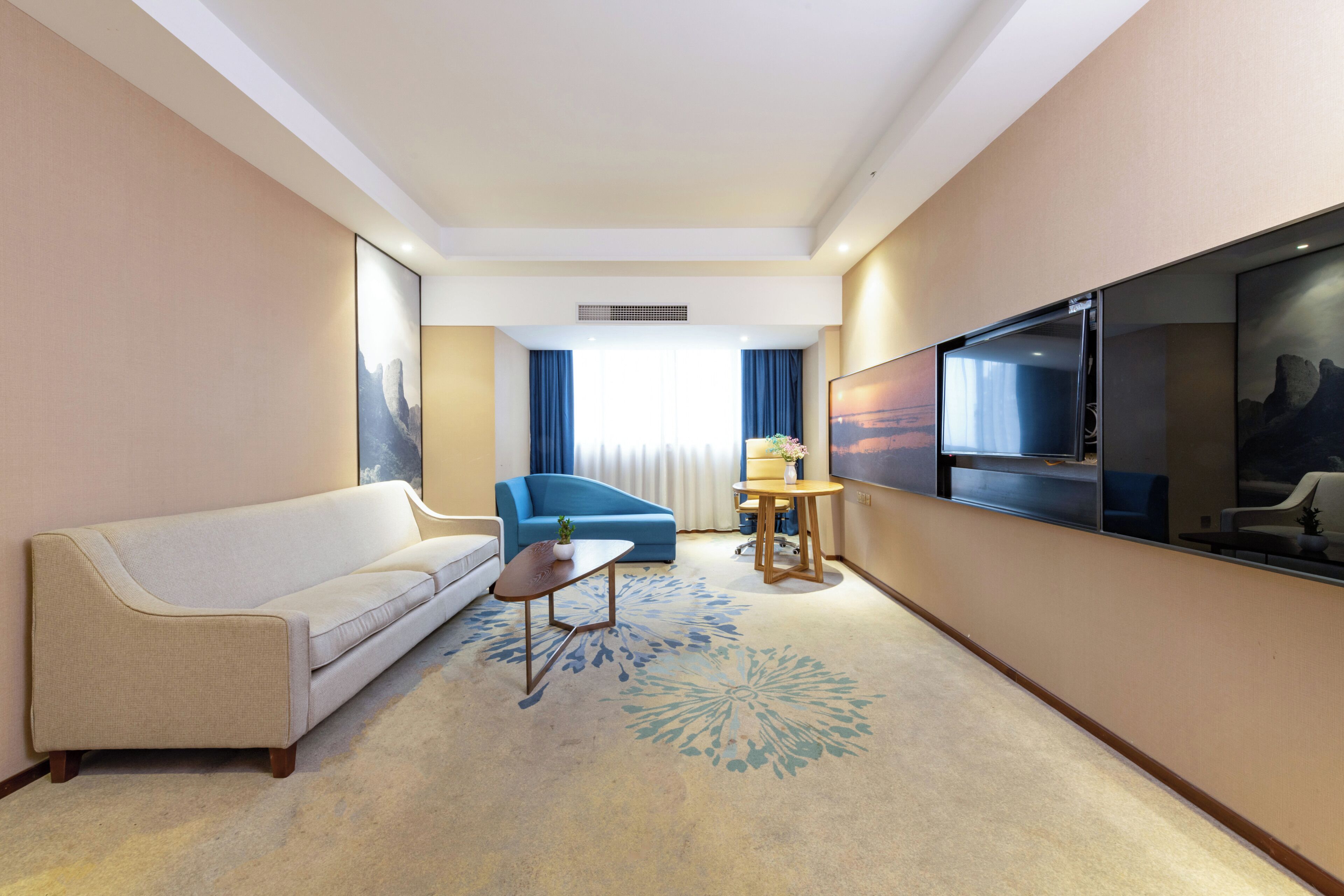 A hotel room with a sofa, a small table, a TV, and a window with curtains.