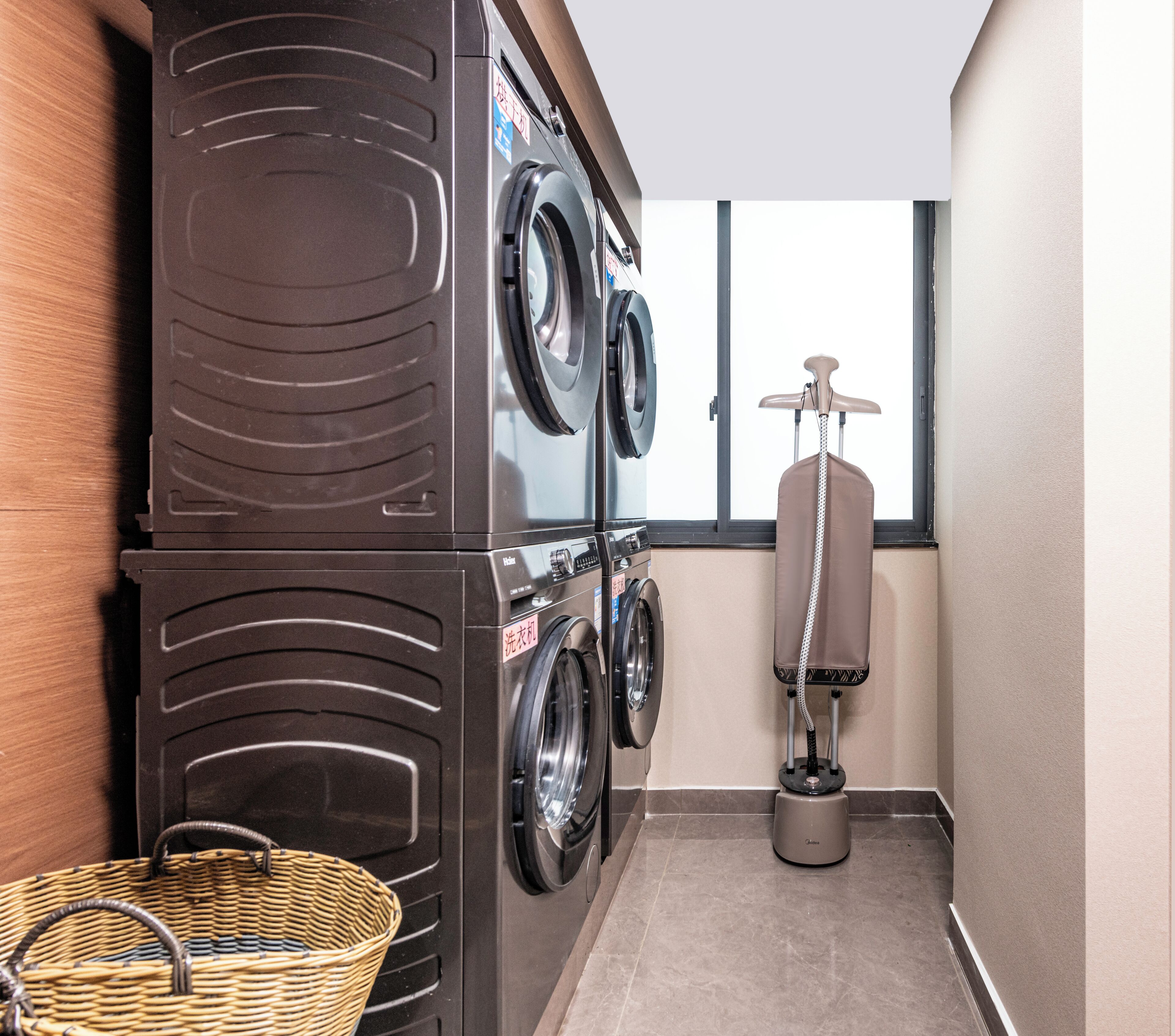 A laundry area with stacked washers and dryers, a drying rack, and a wicker basket.