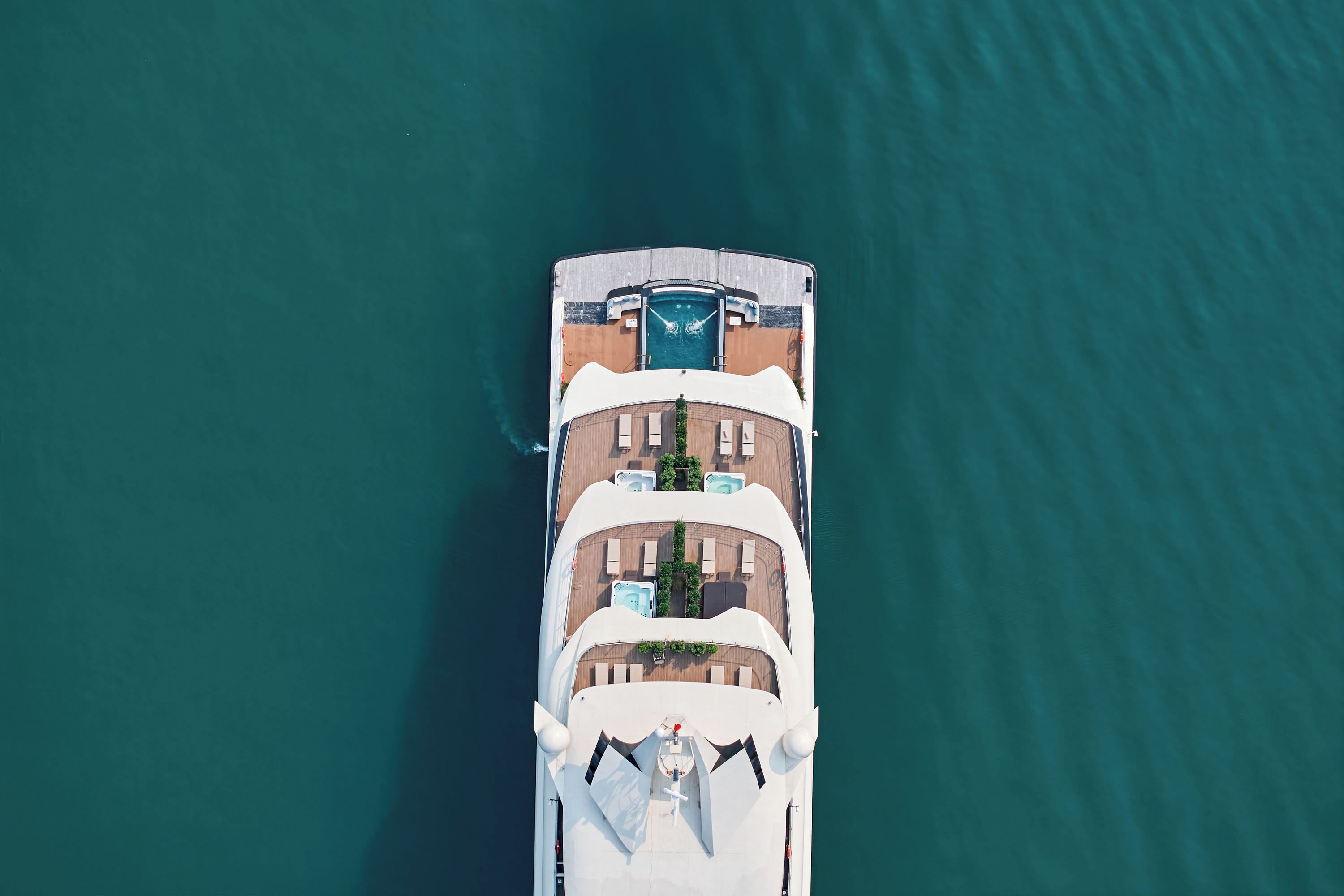 An aerial view of a cruise ship with a pool area, sun loungers, and a deck with a railing.