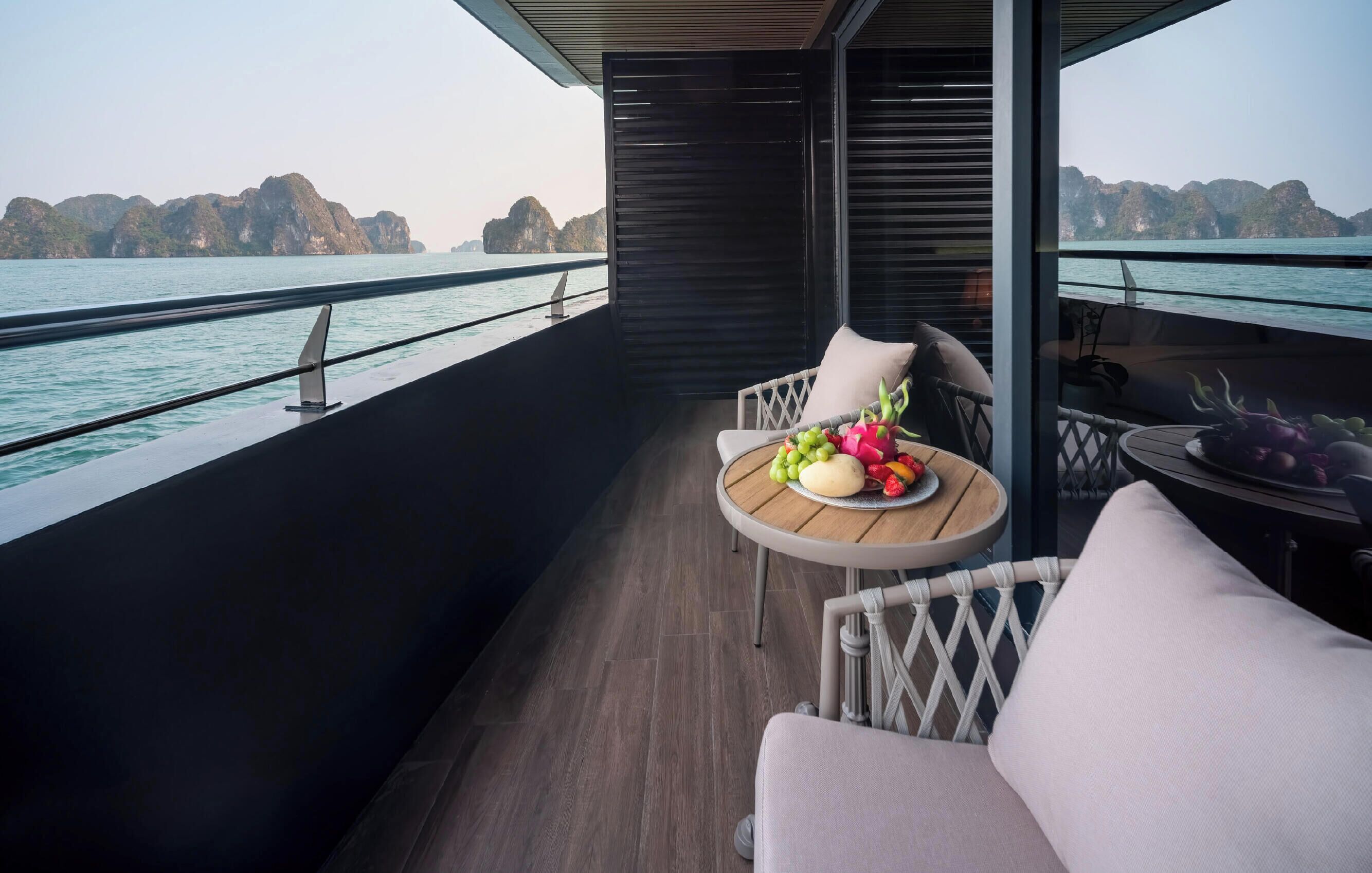A balcony with a table set for a meal, overlooking a body of water and a mountainous landscape.