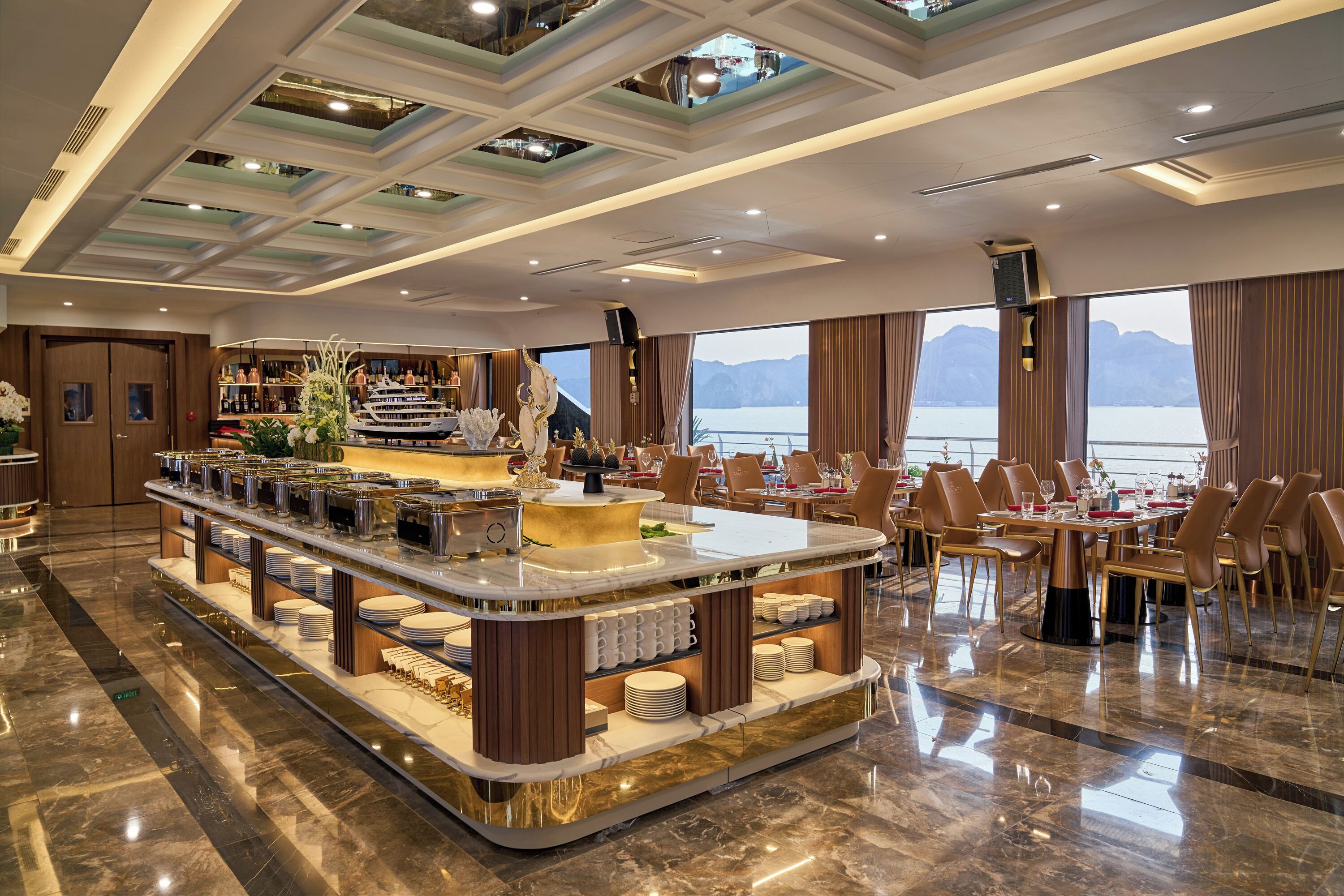 En rummelig hotellobby med et centralt barområde, siddepladser og store vinduer med udsigt til bjergene.