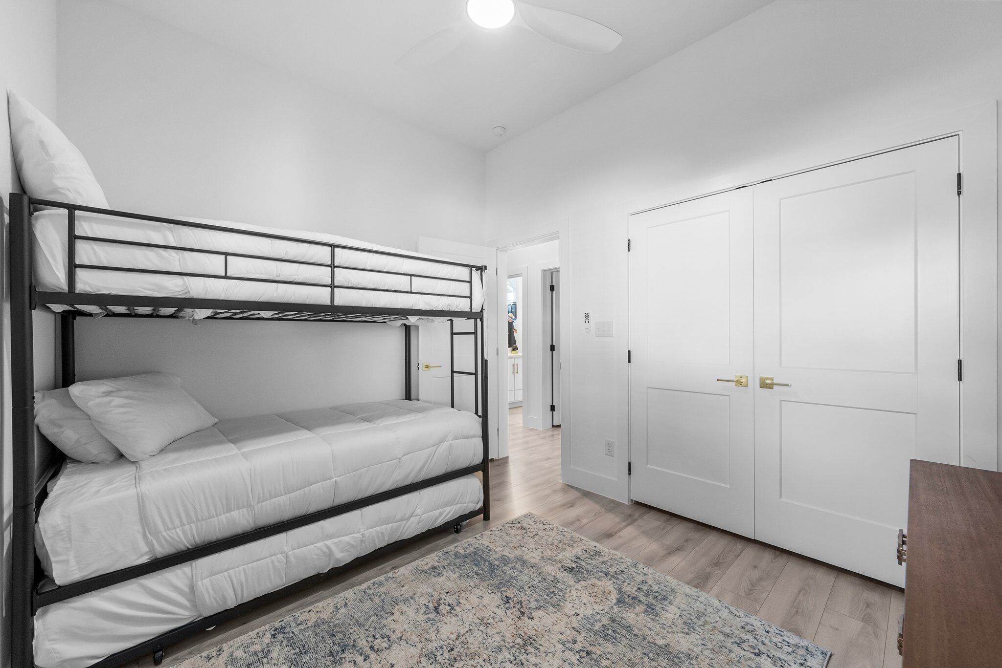 A bunk bed with white bedding, a patterned rug, and a white wardrobe with two doors.