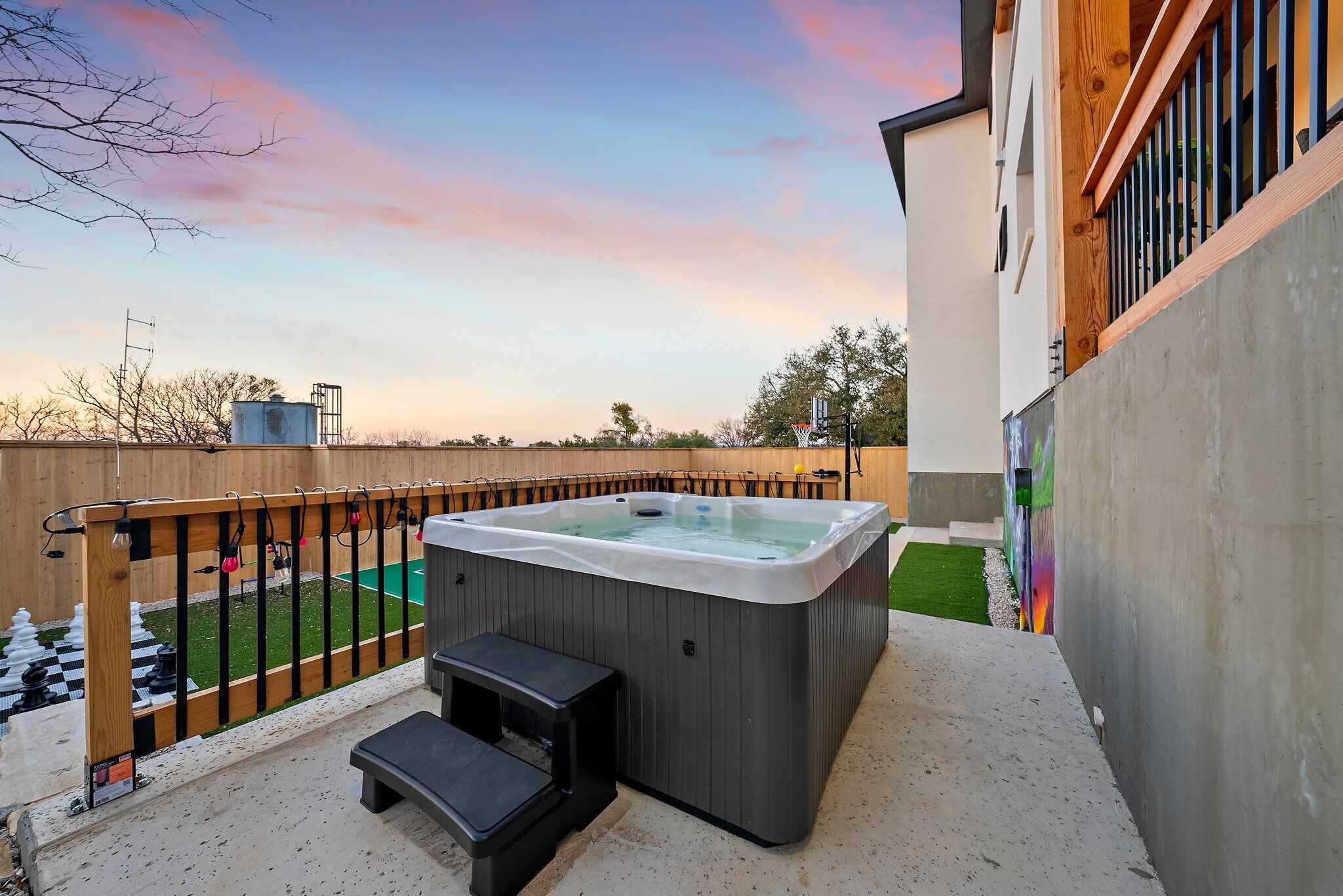 A hot tub in a backyard with a wooden deck, a small step, and a chessboard.