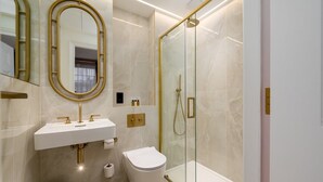 A modern bathroom with a glass-enclosed shower, a white sink with gold fixtures, and a toilet. - GuestReady – Exquisite stay in Fitzrovia (London)
