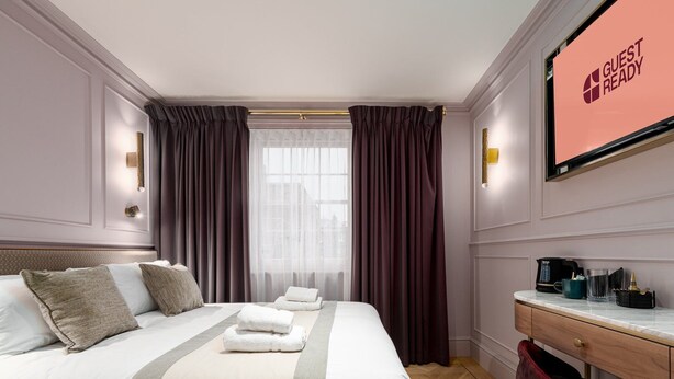 A hotel room with a large bed, a desk with a coffee maker, and a 'Guest Ready' sign. - GuestReady – Exquisite stay in Fitzrovia (London)